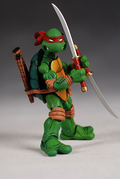a teenage mutant ninja turtle action figure of the character raphael holding a sword, with his shell and red headband.