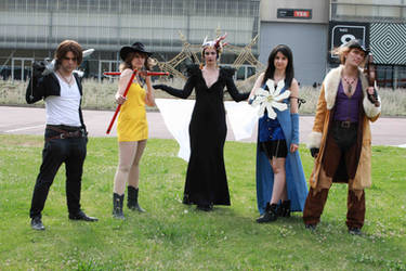 a group of cosplayers dressed as characters from the final fantasy video game series.  they're posing outdoors on a grassy area. the characters include cloud, tifa, sephiroth, zack, and yuffie, each in detailed costumes that accurately represent their ingame appearances.  the setting appears to be a sunny day at a convention or similar event.