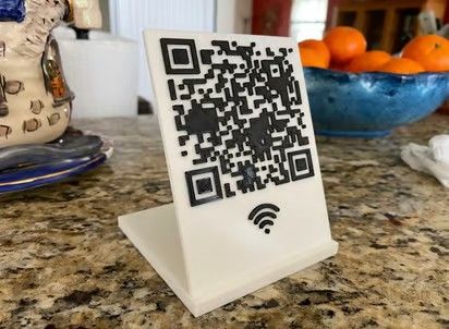 a closeup shot of a white qr code stand on a granite countertop. there are oranges in a blue bowl behind the stand. the qr code has a wifi symbol in the bottom center of the stand.