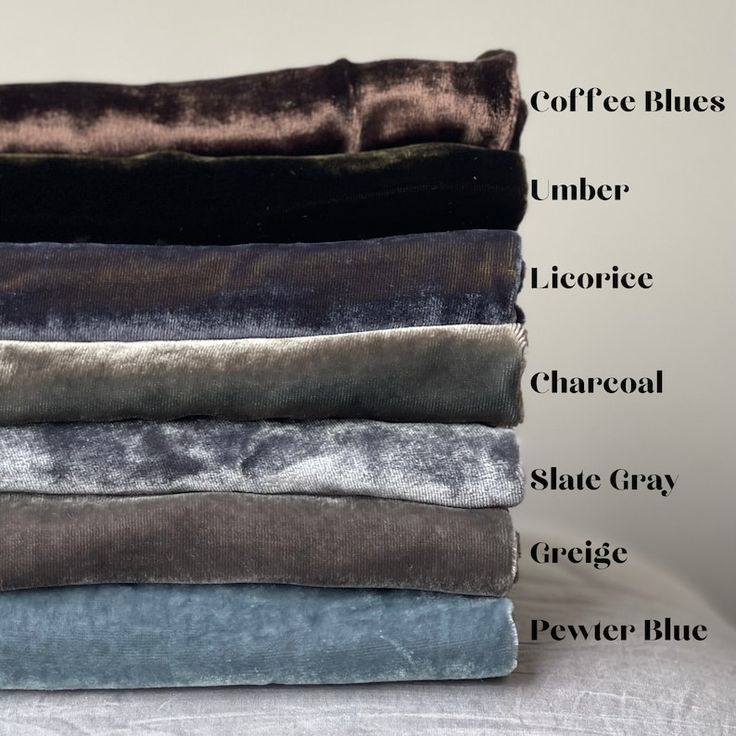 a stack of velvet fabric swatches in a variety of colors, including coffee blue, umber, licorice, charcoal, slate grey, greige, and pewter blue. each swatch is neatly folded and arranged on top of the other, creating a visually appealing display of the different colors and textures of velvet. the light catches the surface of the fabric, highlighting its sheen and luxurious feel.