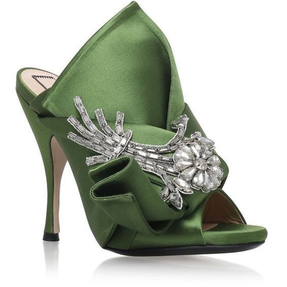 a closeup shot of a pair of women's green satin mules with a large, embellished bow on the vamp. the shoes are highheeled and have a pointed toe. the bow is made of the same satin material as the shoes and is decorated with numerous clear and silver crystals. the shoes appear to be of high quality and are likely designer shoes. the background is plain white, making the shoes stand out.