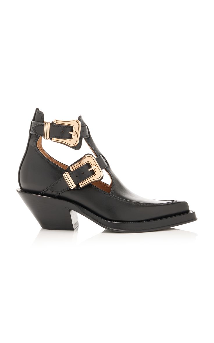 a pair of black leather ankle boots with cutouts and gold buckles are shown in the image.  the boots have a pointed toe and a block heel. they appear to be made of highquality leather. the style is a blend of western and modern, making them a fashionable choice.