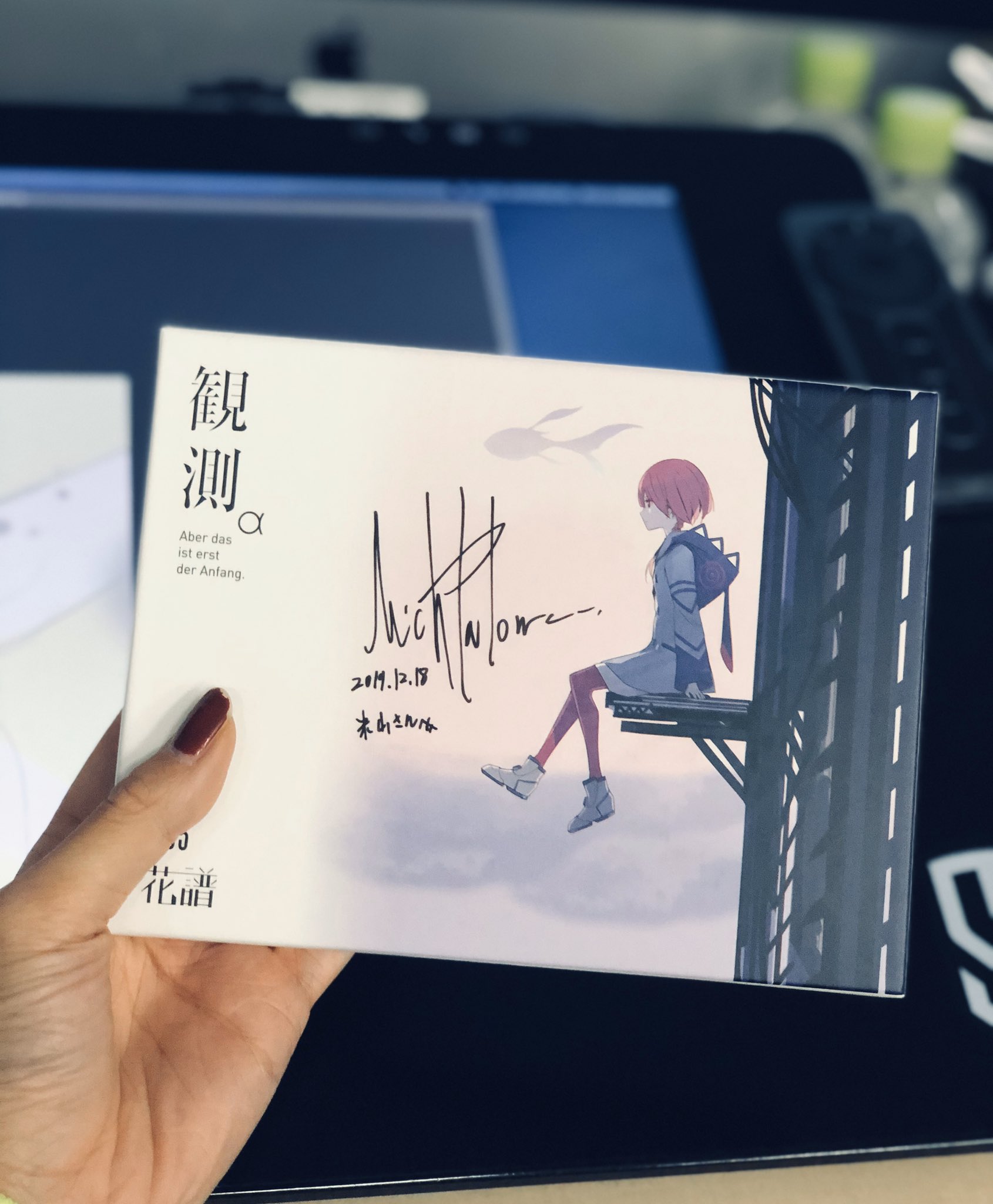 a hand holding a book with a drawing of anime girl on the cover```