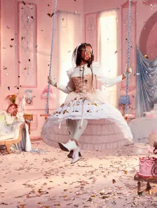 a woman in a white dress with a corset and veil is sitting on a swing in a pink room. confetti is falling around her. there is a cake and bed in the background. a man is sitting in a chair on the left side of the image.