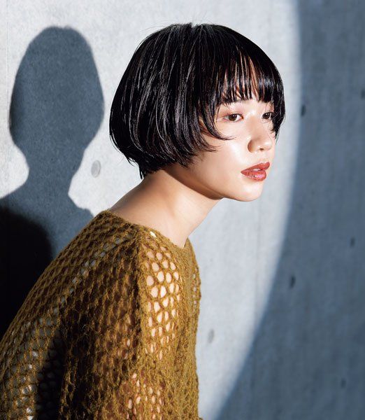 a young asian woman with a bob hairstyle and bangs is wearing a knitted sweater, posing for the camera. she has a casual, chic style, with subtle makeup and a red lipstick.