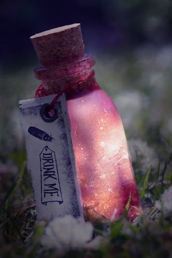 a closeup shot of a vintage glass bottle with a red cork stopper and a label that says "drink me". the bottle is filled with a pink liquid and is resting on a bed of grass. the image has a whimsical and magical feel, like something out of a fairytale.