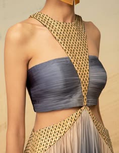 a model poses in a fashionable silver and gold dress. the dress features a blue bodice with gold embroidery and a flowing silver skirt. the dress is very elegant and stylish.