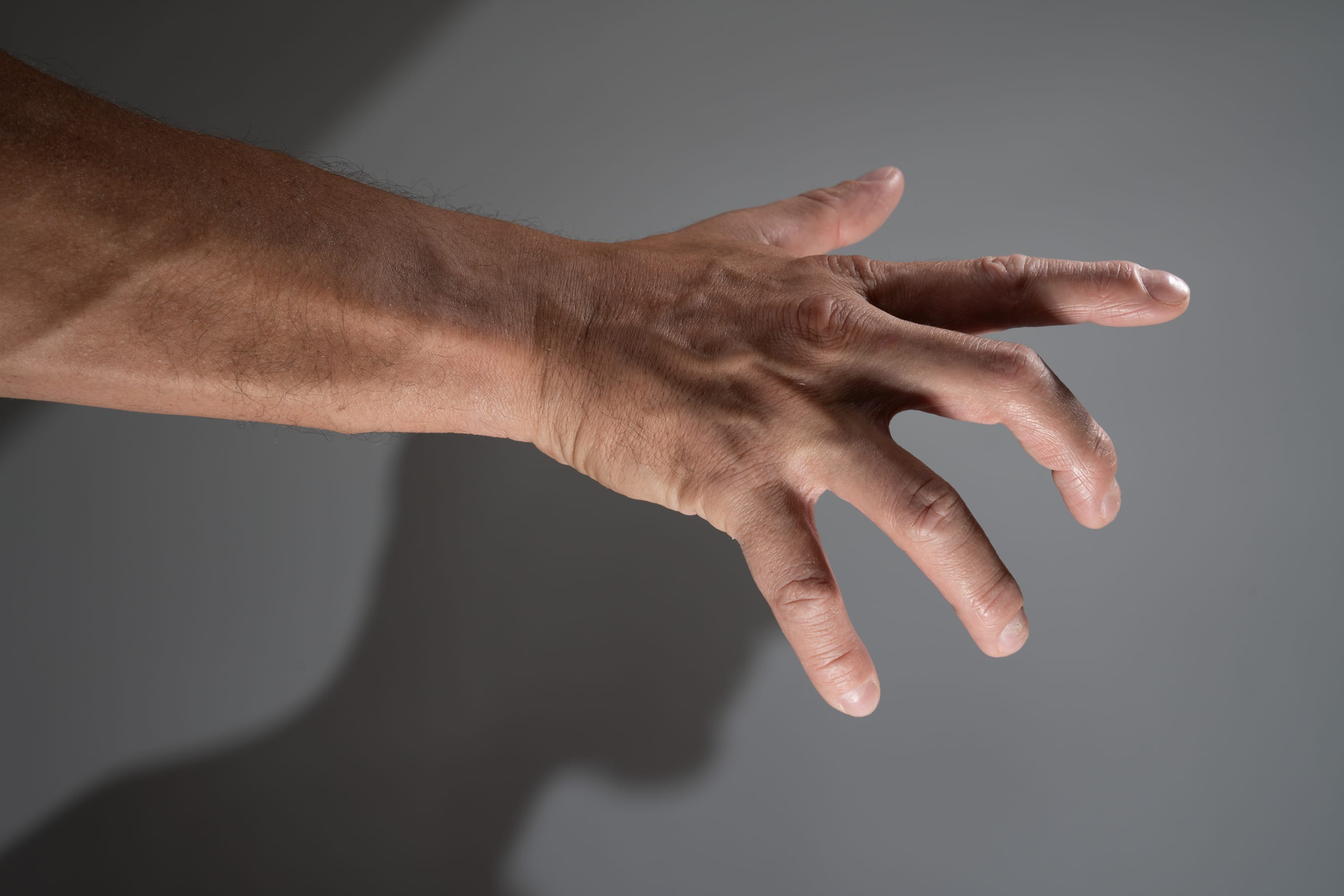 a man's arm and hand extended towards the right side of the image. the background is a solid gray.