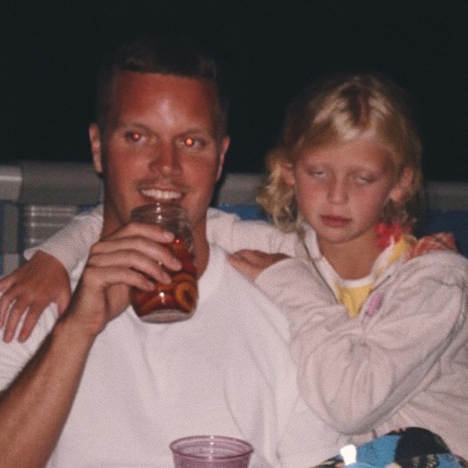 a man is sitting with a child with his arm around her. the man is drinking from a glass.