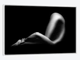 the image is a black and white photograph of a nude female figure reclining. the lighting is dramatic, using strong chiaroscuro to emphasize the curves and contours of the body.  most of the background is pure black, leaving the woman's form silhouetted against it. the focus is on the shape and form of the body, rather than explicit detail. the overall mood is sensual and artistic. the image is simple yet impactful, evoking a sense of elegance and mystery.