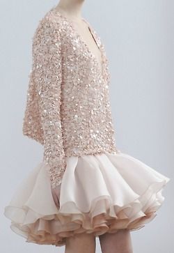a young woman in a sparkly, pink dress is modeling in a studio. the dress is made up of a sequined top and a tulle skirt. the skirt is a mix of ruffles and has a delicate, feminine look. the woman is blonde and has her hair pulled back from her face. she is wearing subtle makeup and has a very elegant look.