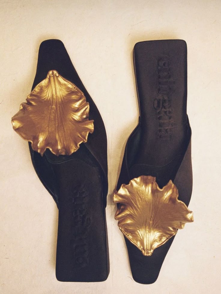 the image shows a pair of black slippers decorated with goldcolored leafshaped ornaments. the slippers are lying next to each other on a light surface. the shoes look luxurious and elegant.