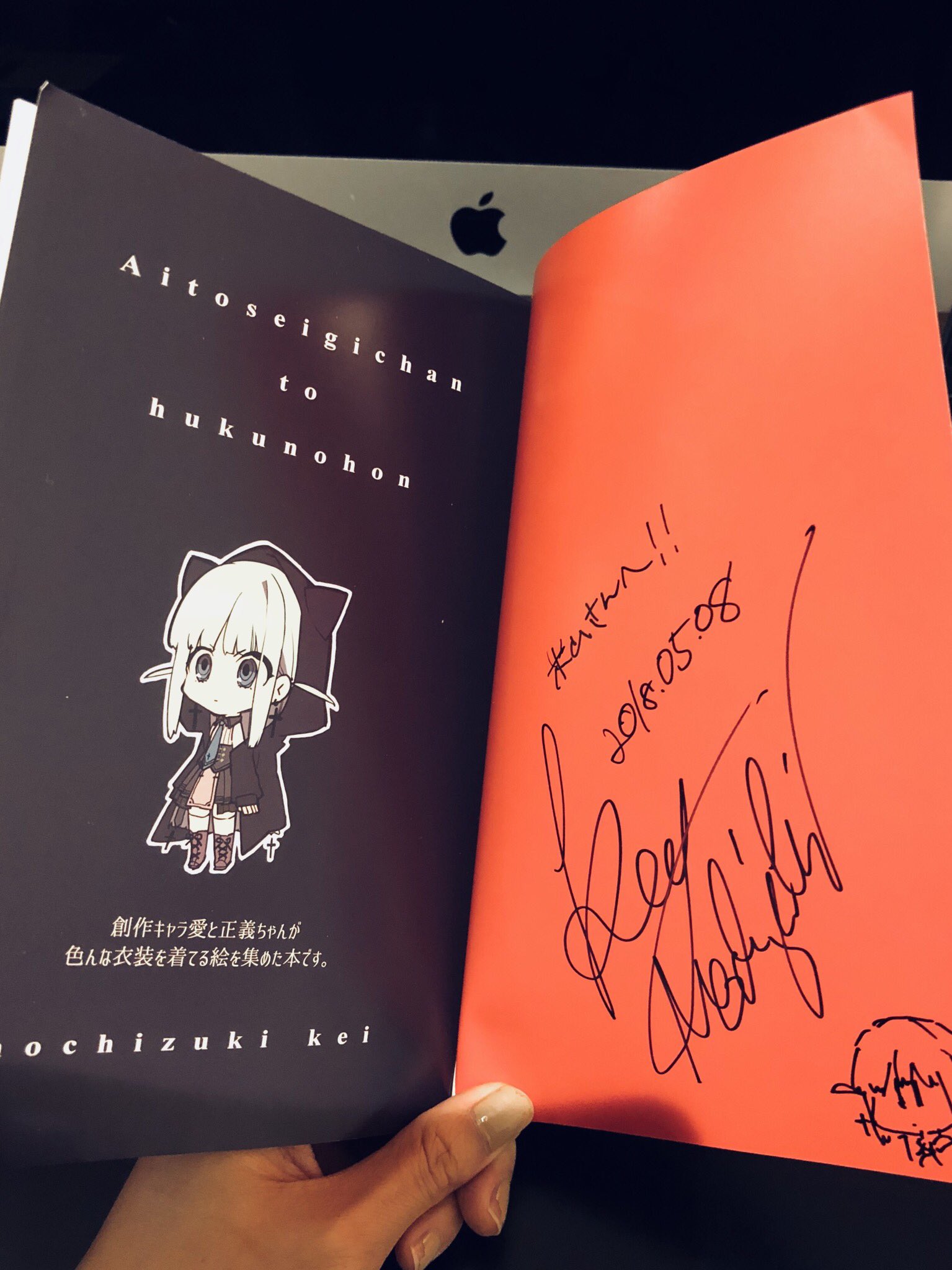 a hand holds up an open book with a visible author's signature on an orange page on the right side of the book. the left side of the book features the cover art and title.
