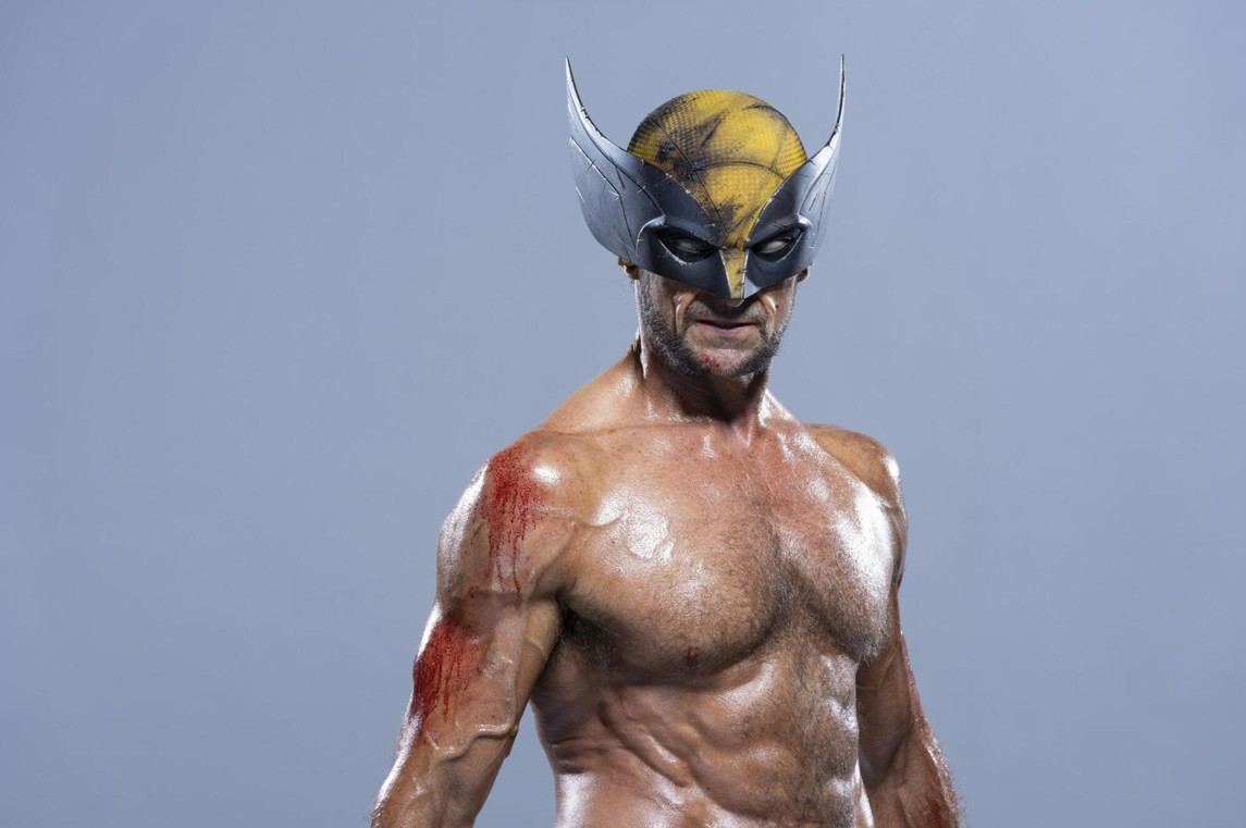 a man with a wolverine mask is standing shirtless. there is blood on his left arm.