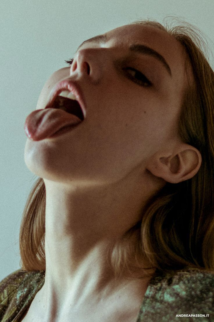 a closeup, lowangle portrait of a woman looking upwards with her mouth open and tongue extended. her face, neck, and ear are visible, as well as a portion of her hair. the image has a sensual quality due to the expression and pose.