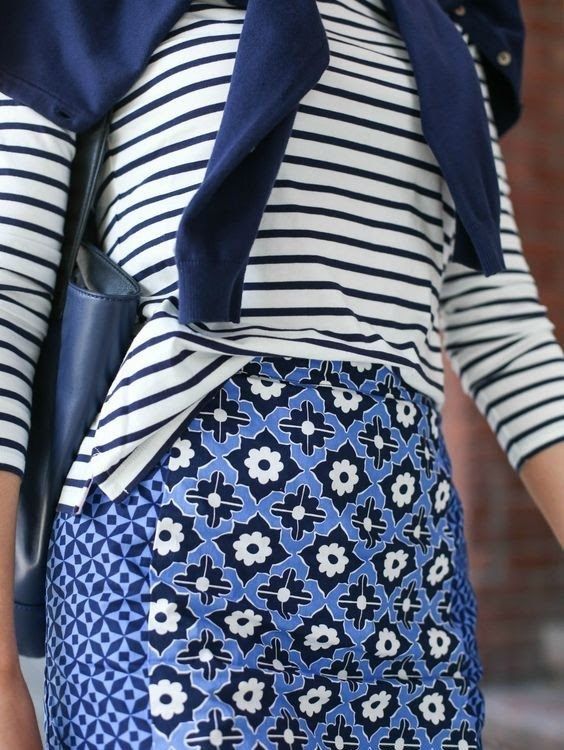 a closeup shot of a woman wearing a navy blue and white striped longsleeved shirt and a blue and white patterned skirt. the skirt features a geometric and floral design. she is also carrying a navy blue tote bag. the overall style is casual and summery.
