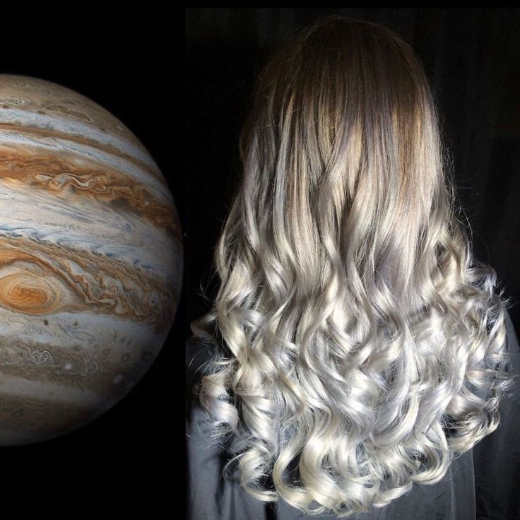a close up portrait of a woman with long, curly silver hair, with a blurred picture of jupiter behind her.  the woman is facing away from the camera, and her hair is styled in a wavy ombre style. the photo is taken against a black backdrop.