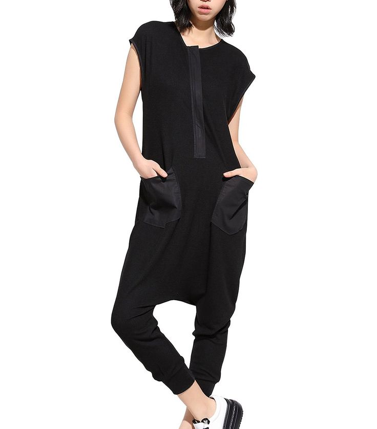 a woman wearing a black capsleeve jumpsuit with large pockets and white shoes is seen in a full shot.