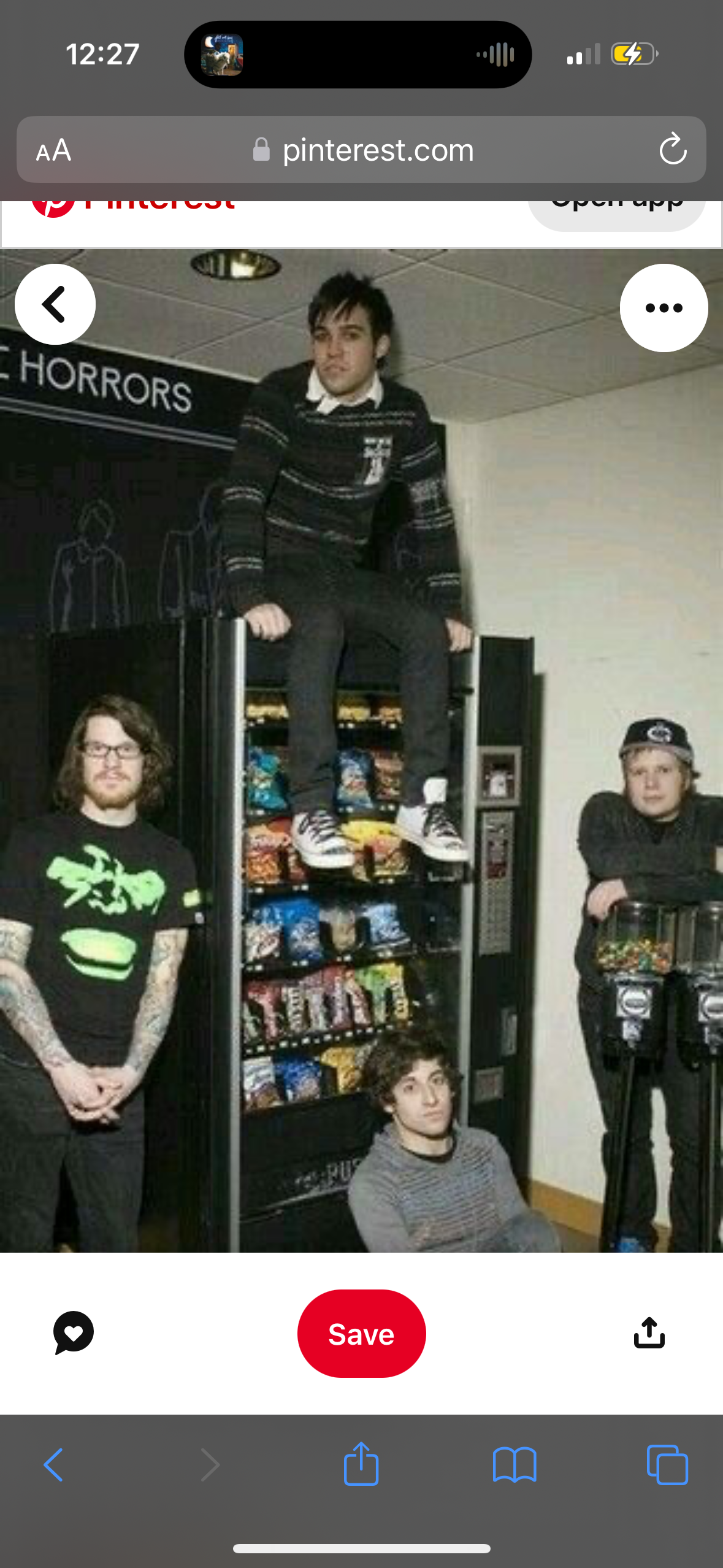 a group of four young men stand and sit in front of a vending machine. one man sits on top of the machine while the others stand around it. they look to be having fun together.