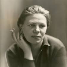 a black and white closeup portrait of a woman with her hand to her face. she appears to be holding a cigarette. the image is slightly grainy, suggesting it may be an older photograph. the woman has a serious expression.  she has her hair pulled back and wears a simple, darkcolored collared shirt or jacket. the background is blurred and indistinct.  the overall style is reminiscent of mid20th century portrait photography.