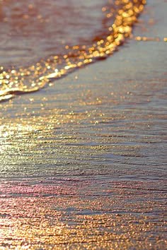 a close up of a wave crashing on the sandy shore, the sunlight reflecting off the water to make it shimmer and sparkle.