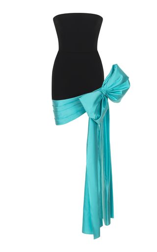 a strapless black cocktail dress has a large turquoise bow on one side with a long sash hanging down.