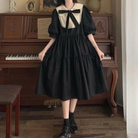 a young woman is posing indoors, wearing a black vintageinspired dress. the dress features a white peter pan collar with a black bow tie, puffed sleeves, and a flowy midi skirt. she is standing in front of a classic piano, with a framed picture and a mirror visible in the background. the lighting is slightly dim, giving the image a cozy and nostalgic feel.