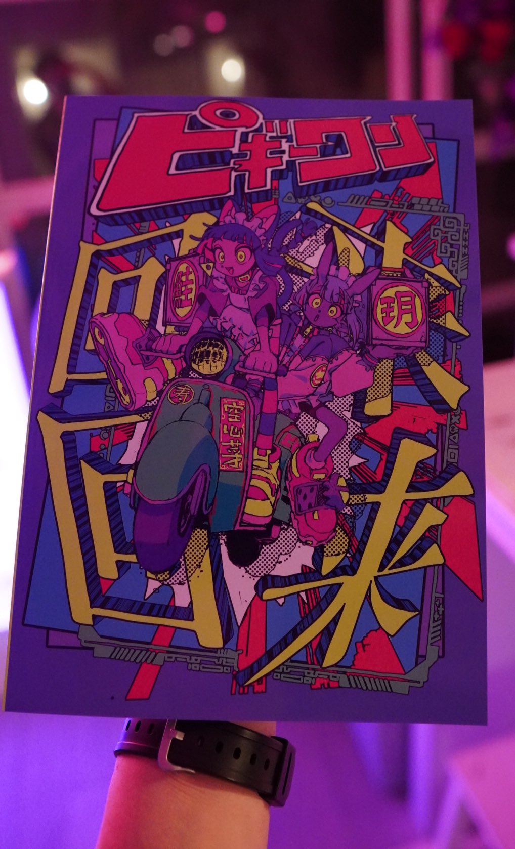 a hand holding up a comic book with a purple background. the cover art of the comic is two girls riding a motorcycle in a cityscape. the style is animeinspired with bold lines, bright colors, and exaggerated features.