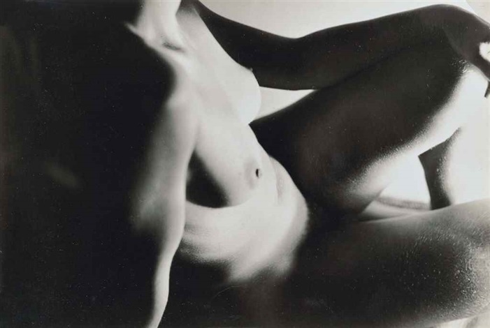the image is a black and white photograph of a nude female figure. the subject is positioned in a seated or reclined pose, with her body angled toward the viewer. the lighting is dramatic, using strong contrasts between light and shadow to emphasize the curves and forms of the body. the photograph focuses primarily on the torso, legs and upper body, with the face obscured. the overall style is artistic and somewhat abstract, using light and shadow to create a sense of mood and atmosphere. the texture of the skin is also subtly visible due to the high contrast.