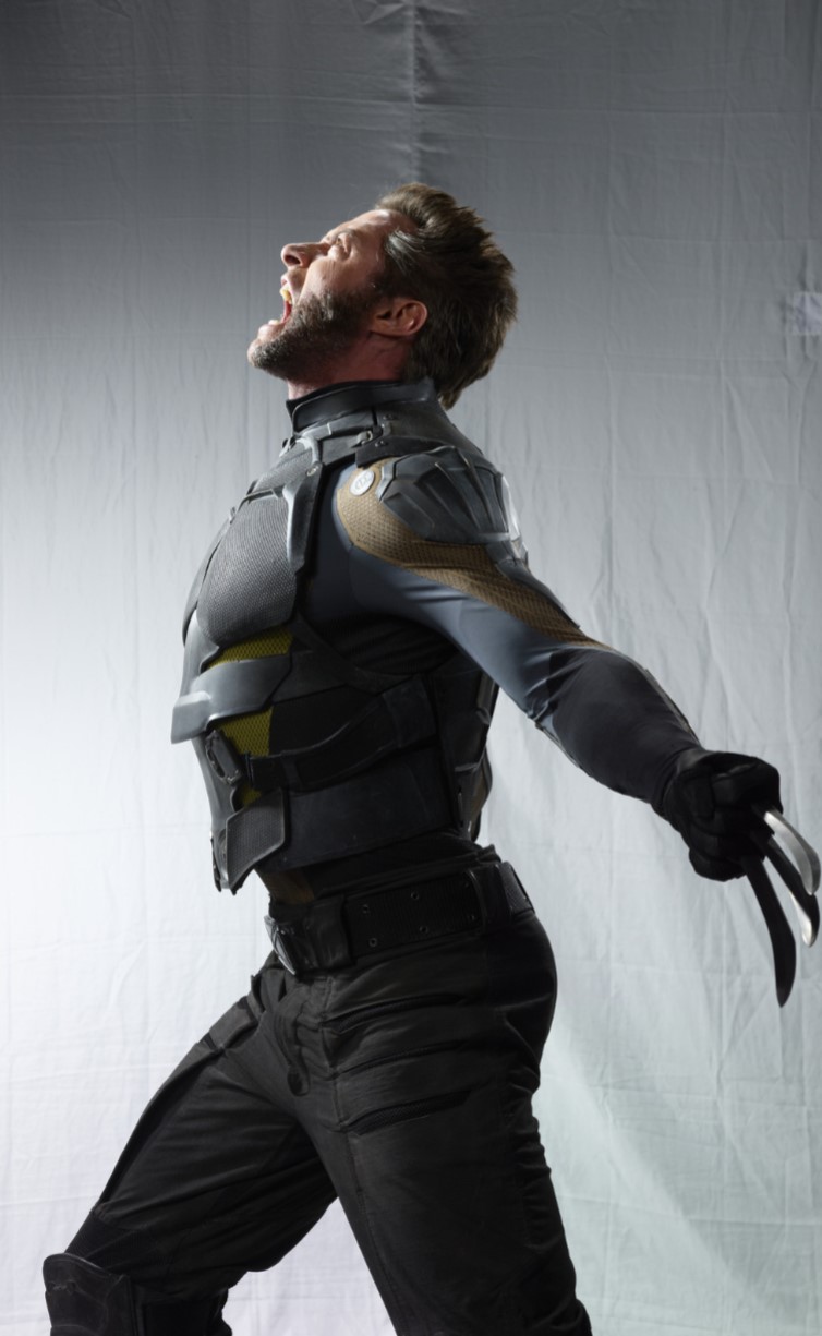 a fullbody shot of hugh jackman as wolverine in costume, yelling with his claws extended. the image is a side view against a plain white/grey background.