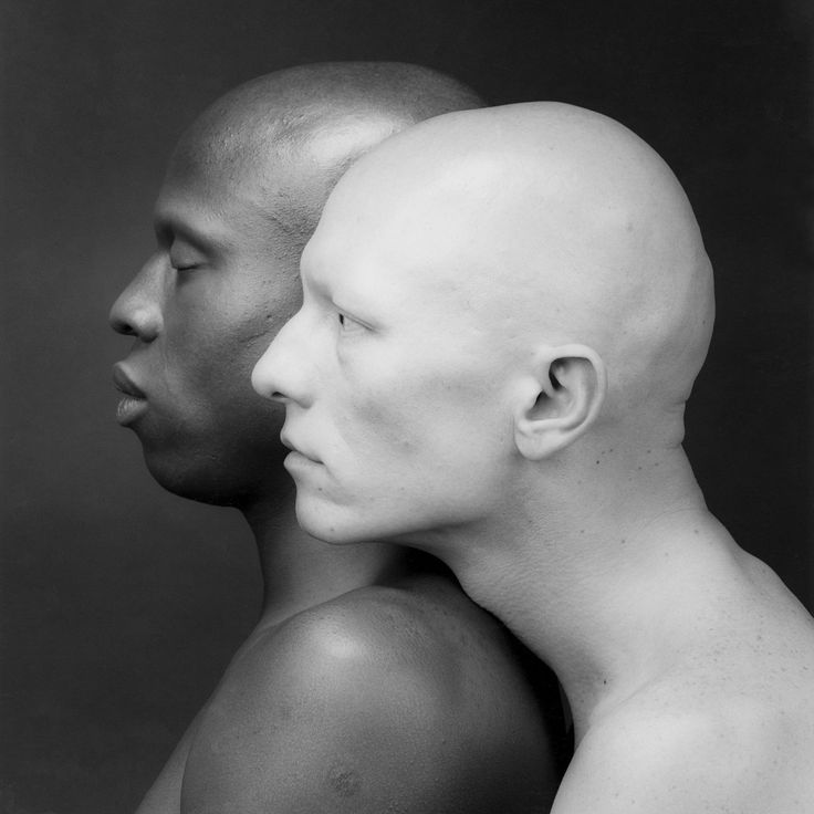 a black and white portrait of two men, one black and one white, standing back to back, their heads close together. the image focuses