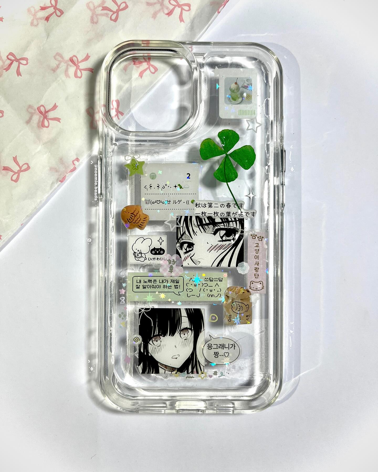 a clear phone case decorated with manga panels, stickers, a clover, and text in korean and japanese languages.