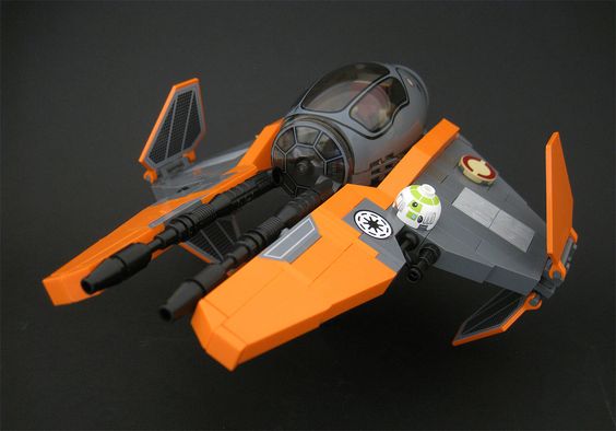 a lego star wars model of a starfighter with orange wings and a gray body. there is a minifigure of obiwan kenobi in the cockpit and an r4p17 astromech droid behind him. the model is set against a dark gray background and lit with studio lighting.