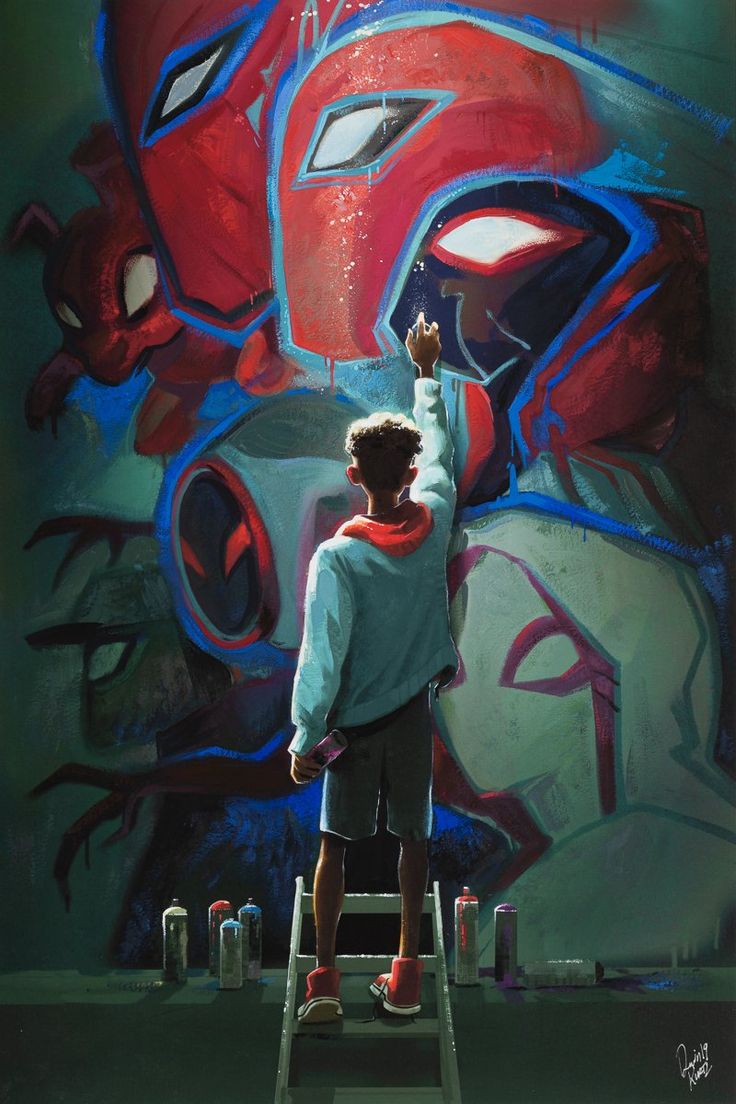 a young man is spraying red paint on a wall mural of spiderman with a spray paint can in his hand. he is standing on a ladder and there are spray paint cans on the ground next to the ladder.  the wall is covered in graffiti and the light is coming from the top of the image. it is dusk and the scene is urban.