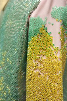 close up shot of a green and yellow fabric with a beaded pattern. the fabric is made of sequins and looks to be a design from a fashion item such as a dress or jacket.