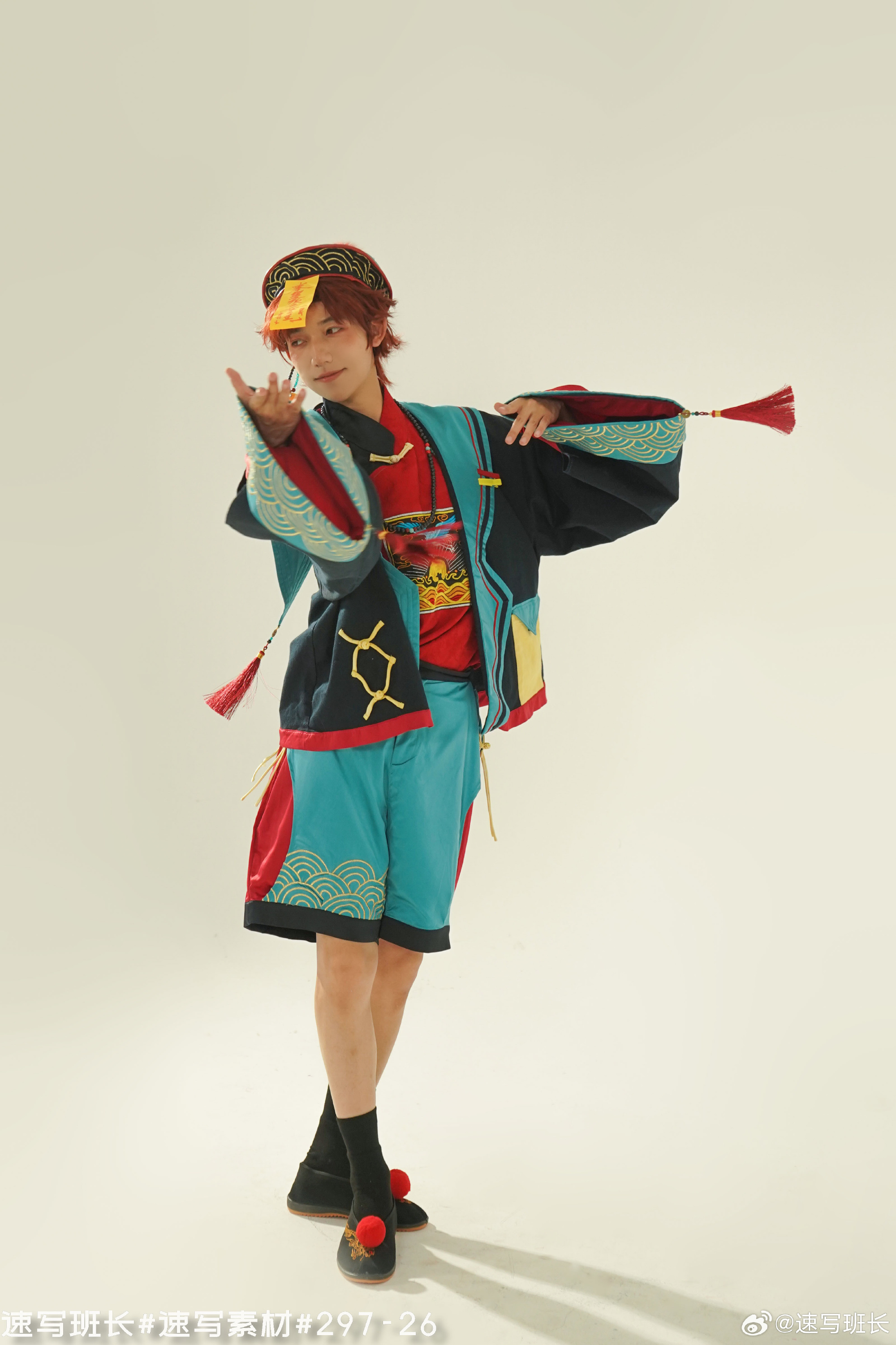 a young man wearing a vibrant and colorful traditional chineseinspired costume stands in a dancing pose against a white studio backdrop. the costume features shades of blue, green, red, and black, with intricate embroidery and patterns. the man's pose and expression convey a sense of energy and movement.