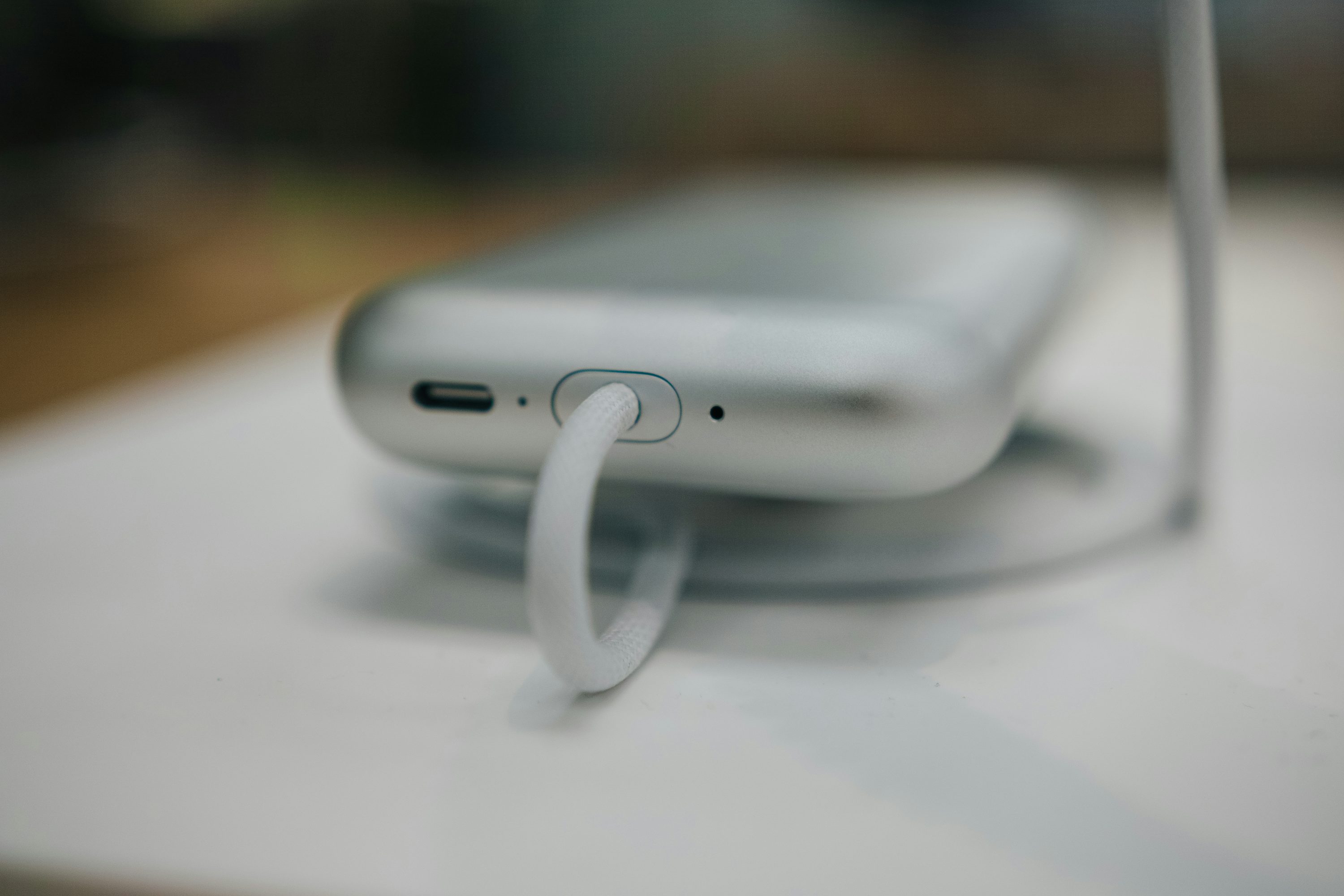 a closeup shot of a pair of silver wireless headphones resting on a white surface. a white cable is attached to one of the headphones. the image has a modern and minimalist aesthetic.