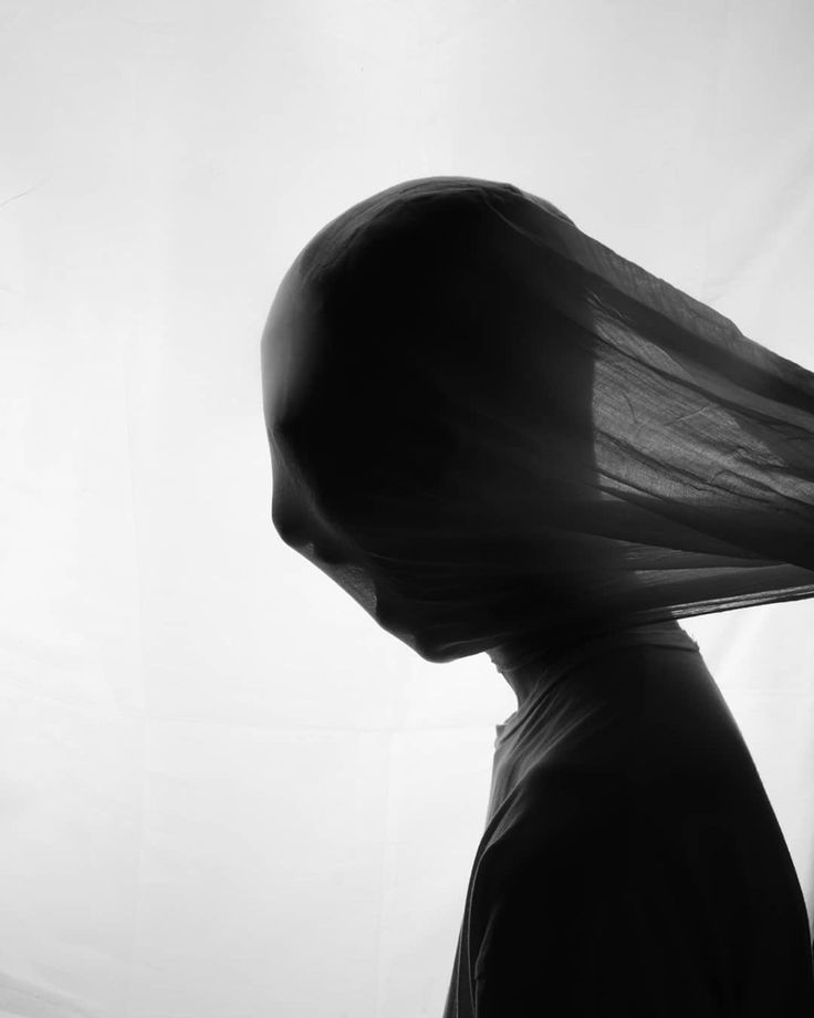 a black and white image of a person, with their head covered by a cloth and the rest of their body in silhouette. the person is facing away from the camera. the photo has a very abstract feel to it.