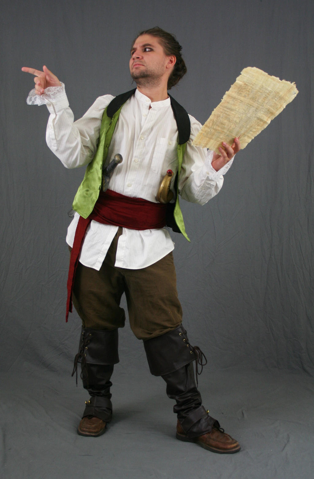 a fullbody shot of a man dressed in a pirate costume. he is wearing a white shirt, a green vest, brown pants, and brown boots. he has a red sash around his waist and carries a scroll. he is posing against a gray background.