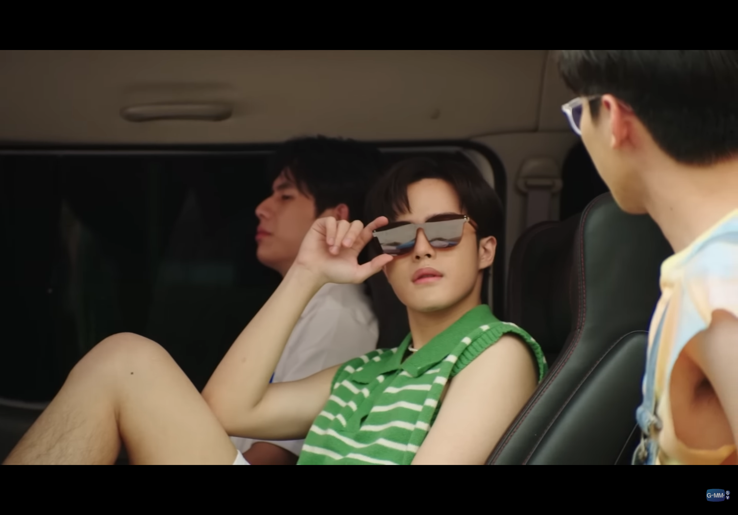 three young men are captured inside a vehicle, likely on a road trip. the focus is on the man in the center, who is adjusting his sunglasses with a confident air. he wears a stylish green striped shirt and exudes a sense of summery coolness.  the man on the left, dressed in white, appears relaxed, while the person on the right remains partially obscured. the overall atmosphere is carefree and suggestive of a fun, shared experience.