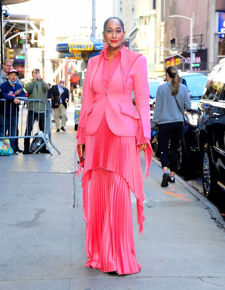 tracee ellis ross is seen on a city street wearing a striking pink suit with a matching pleated skirt. she is surrounded by paparazzi and onlookers, indicating a public appearance. the photo captures the daytime setting and the overall fashionforward look of the celebrity.
