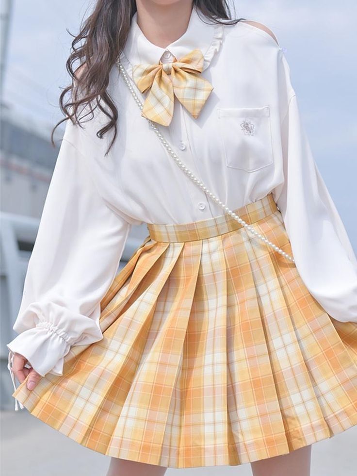 a woman is standing outside wearing a white blouse with a bow tie and a yellow plaid pleated skirt. she is also wearing a pearl necklace. the photo is taken from the waist up. the lighting is soft and the perspective is at eye level.