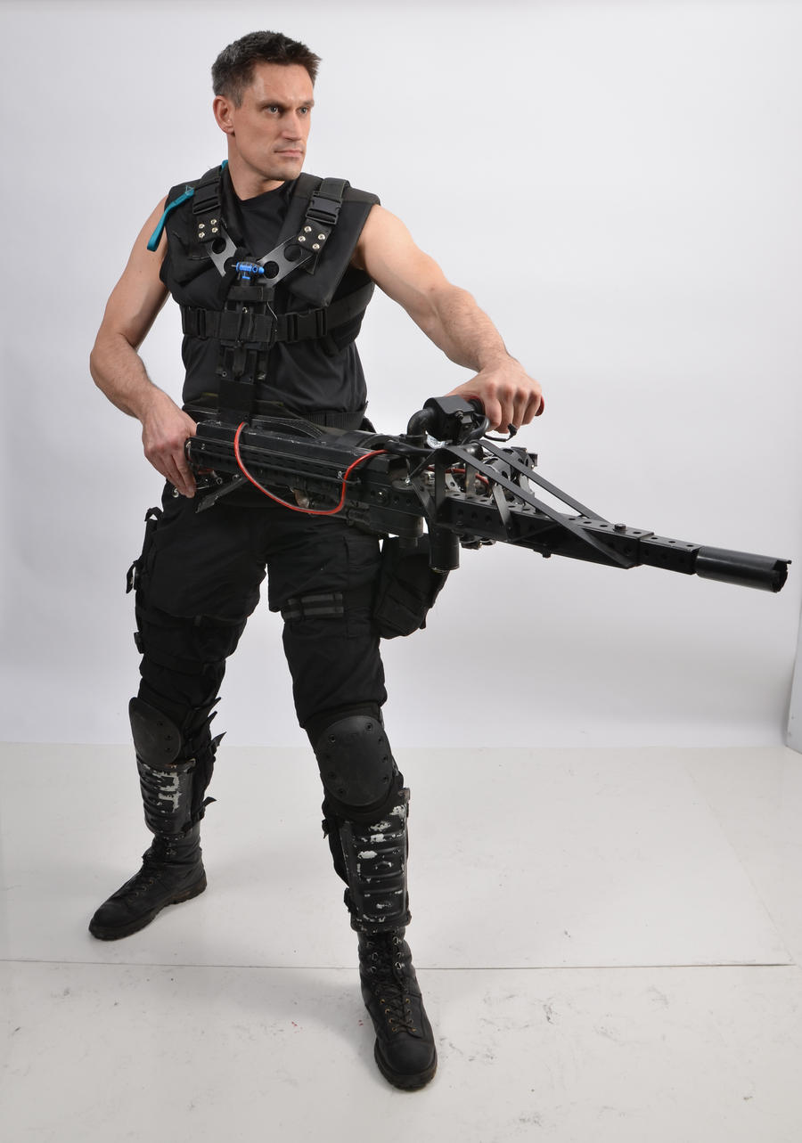a full shot of a man dressed in tactical gear, including a vest, knee pads, and boots, holding a large, futuristic weapon. he is posing against a white background. the man appears to be a soldier or character from a scifi setting.  the image is well lit and professionally taken, suggesting it may be a stock photo or promotional material.