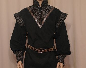 a man wearing a medieval costume with a long black tunic with silver and gold accents.  the tunic has a high collar, long sleeves, and a silver and gold belt. the man's face is not visible in the image. the background is plain and beige.