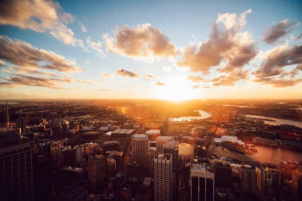 aerial view of a city skyline at sunset with clouds in the sky and a river running through the urban landscape. the buildings are silhouetted against the golden light of the setting sun.
