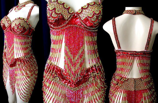 the image shows a red and gold beaded dress on mannequins. the dress is heavily embellished with sequins and beads, with a halter top and beaded fringe. there is a matching necklace and choker. the mannequins are positioned against a black background. the dress is a belly dance costume.