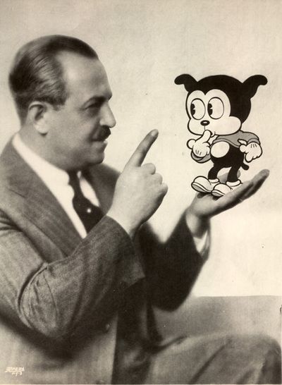 the image is a black and white portrait of grim natwick, the creator of betty boop,  posing with an illustration of the iconic cartoon character.  natwick is pointing to betty boop with his right hand as he looks at her with an amused expression. the photo appears to be taken in a studio setting with professional lighting.