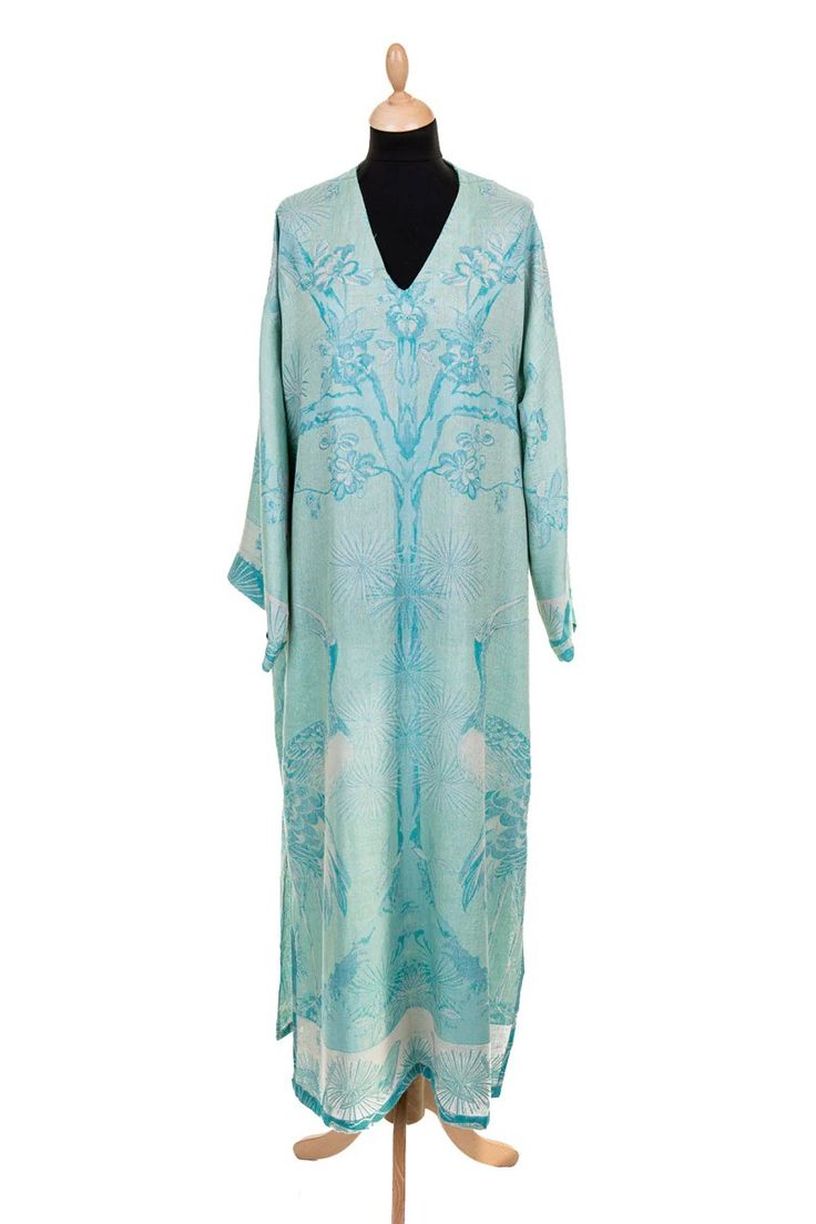 a long, flowing dress in a light blue color with a floral and peacock pattern. the dress is made of silk and has a vneckline and long sleeves. the dress is displayed on a mannequin.