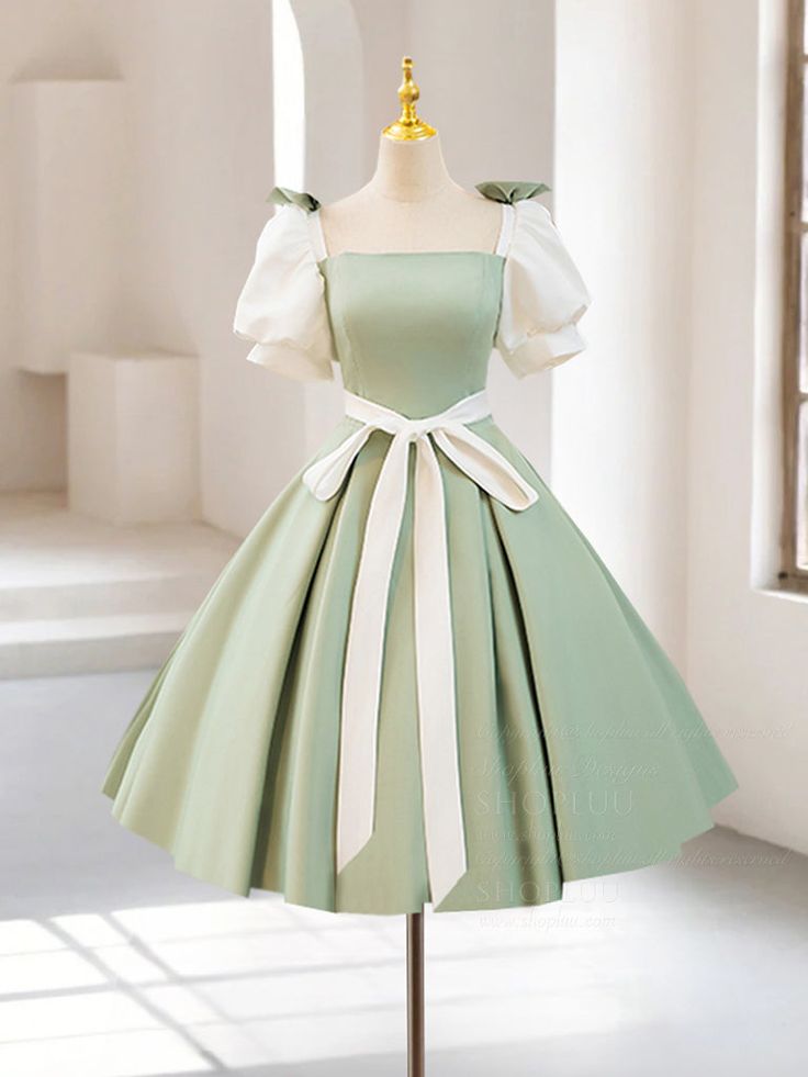 the image showcases a stylish green and white dress displayed on a mannequin in what seems to be a welllit studio or showroom. the dress boasts a charming vintage aesthetic, featuring a square neckline, elegant puff sleeves, and a flowing aline skirt that falls gracefully to tea length. a wide white ribbon accentuates the waist, adding a touch of sophistication.  the light green hue of the dress exudes a fresh and springlike appeal. the backdrop features clean white walls and a glimpse of a window, suggesting a bright and airy setting.