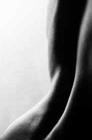 the image is a black and white closeup photograph of a person's back, showcasing the curves and texture of the skin. the lighting creates strong shadows and highlights, emphasizing the body's form. the overall tone is sensual and artistic.  the focus is on the anatomical details and the aesthetic quality of the form.